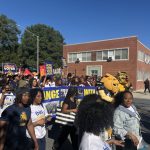 NC A&T campus polling site march with students carrying voter signs and university mascots on a sunny street