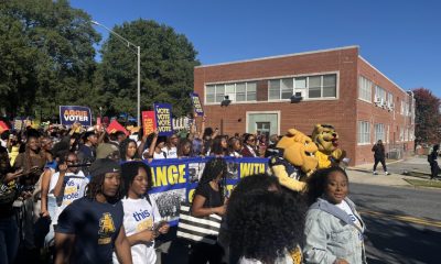 NC A&T campus polling site march with students carrying voter signs and university mascots on a sunny street