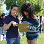 Two young women discussing and reviewing a clipboard outdoors, surrounded by a group of p — Gen Z abortion ballot measures