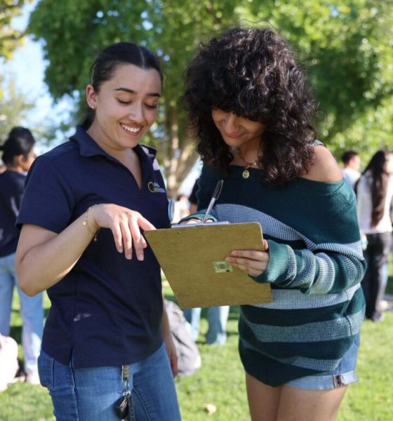 Two young women discussing and reviewing a clipboard outdoors, surrounded by a group of p — Gen Z abortion ballot measures