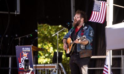 Musician performing at a No Kings early voting day of action event, with an American flag in the background.