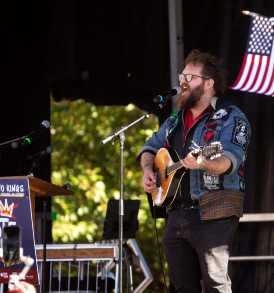 Musician performing at a No Kings early voting day of action event, with an American flag in the background.