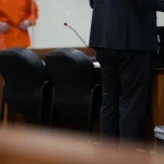 A defense attorney stands at a table in a courtroom while a client in an orange jumpsuit — Texas public defender shortage