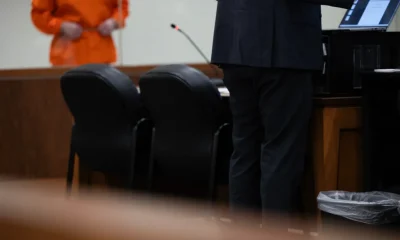A defense attorney stands at a table in a courtroom while a client in an orange jumpsuit — Texas public defender shortage