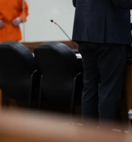 A defense attorney stands at a table in a courtroom while a client in an orange jumpsuit — Texas public defender shortage