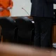 A defense attorney stands at a table in a courtroom while a client in an orange jumpsuit — Texas public defender shortage
