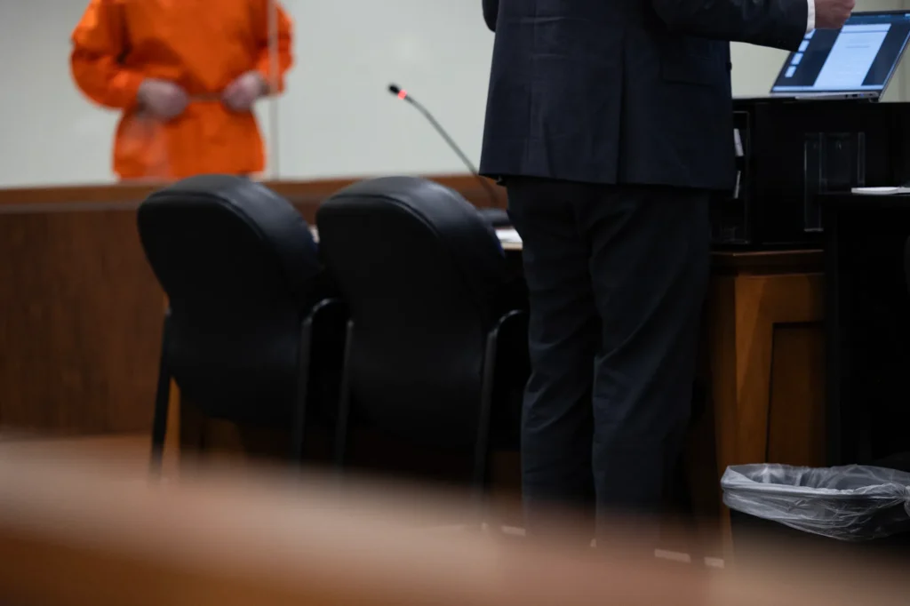 A defense attorney stands at a table in a courtroom while a client in an orange jumpsuit — Texas public defender shortage