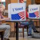 Voters cast ballots at privacy booths marked “I Voted,” illustrating Ballot Measure Reading Level concerns.