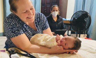A midwife cradles a newborn beside a masked caregiver; states without birth centers face gaps in maternal care.
