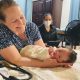 A midwife cradles a newborn beside a masked caregiver; states without birth centers face gaps in maternal care.