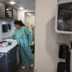 Healthcare worker in teal scrubs handles supplies in a clinical room, illustrating the rising uninsured rate in US.