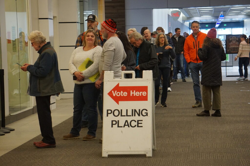 Voters queue inside a public building beside a “Vote Here” polling place sign, amid Trump DOJ election lawsuits.