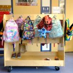 Colorful backpacks hanging on a wooden rack in a school hallway, representing educa — Education Freedom Tax Credit program
