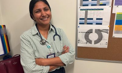 Smiling female doctor with a stethoscope, standing in front of a bulletin boa — Trump Immigration Policies Foreign Doctors