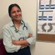 Smiling female doctor with a stethoscope, standing in front of a bulletin boa — Trump Immigration Policies Foreign Doctors