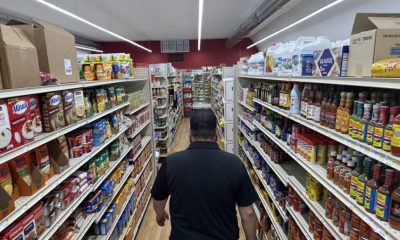 A shopper walks down a grocery aisle lined with shelves of packaged food, illustrating the Rising Cost of Living Midterms.