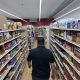 A shopper walks down a grocery aisle lined with shelves of packaged food, illustrating the Rising Cost of Living Midterms.