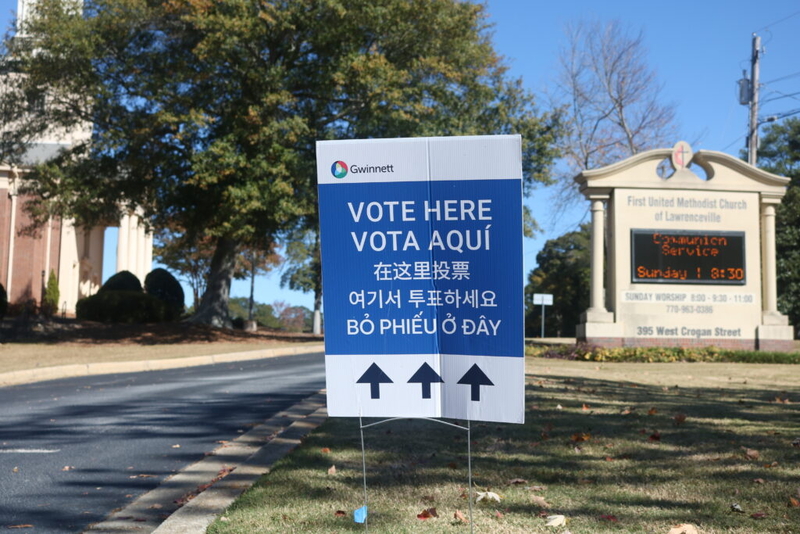 DHS naturalized citizen voter lawsuit context: multilingual “Vote Here” sign outside a church polling place.