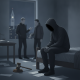 A hooded figure sits on a bed in a dimly lit room, while two indistinct figure — New York sexual consent intoxication laws