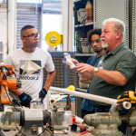 Instructor demonstrates pipe fitting to students in workshop — New Home Construction Decline