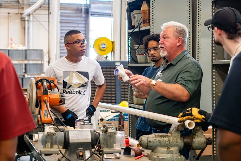 Instructor demonstrates pipe fitting to students in workshop — New Home Construction Decline