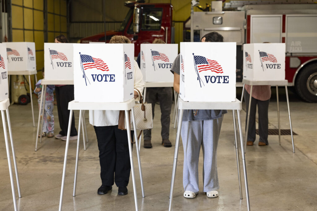 Voters stand at white voting booths with American flag and “I Vote” signs; DOJ Election Subpoenas Los Angeles County i…
