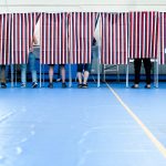 Voters casting ballots behind striped privacy screens in a gymnasium during an election. — Trump voter rolls lawsuit