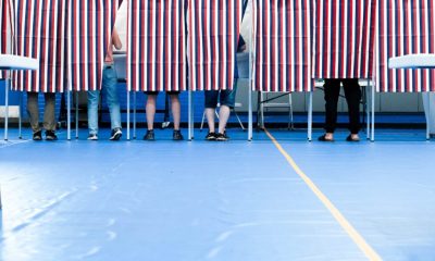 Voters casting ballots behind striped privacy screens in a gymnasium during an election. — Trump voter rolls lawsuit