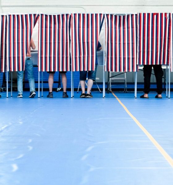 Voters casting ballots behind striped privacy screens in a gymnasium during an election. — Trump voter rolls lawsuit