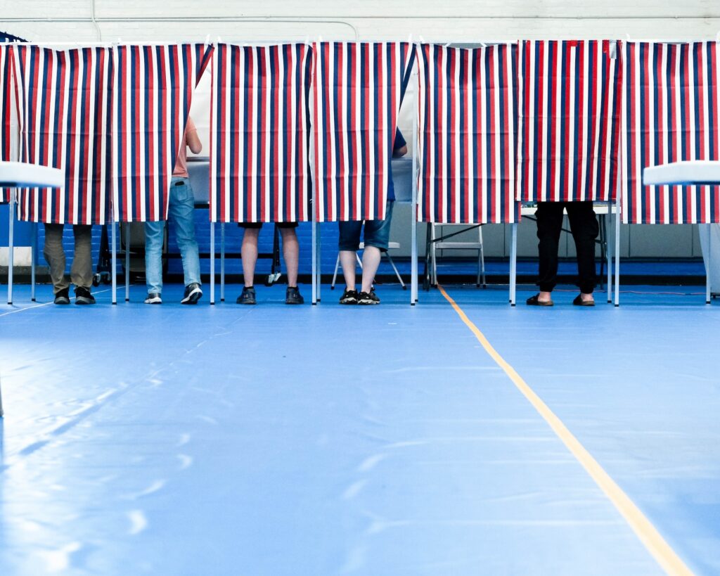 Voters casting ballots behind striped privacy screens in a gymnasium during an election. — Trump voter rolls lawsuit