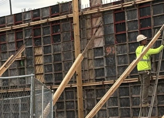 Construction worker in a bright yellow shirt working on a concrete form at a building site — skilled trade worker shortage