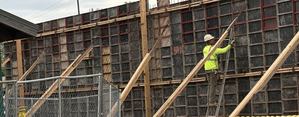 Construction worker in a bright yellow shirt working on a concrete form at a building site — skilled trade worker shortage