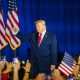 Former President Trump raises his fist in front of a crowd, with America — Federal Election Interference Midterm Elections