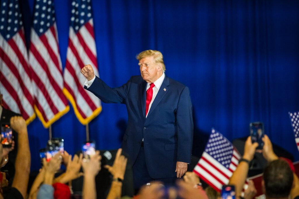 Former President Trump raises his fist in front of a crowd, with America — Federal Election Interference Midterm Elections