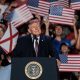 Donald Trump speaking at a rally with supporters holding American flags, promoting mail- — Trump encourages mail-in voting