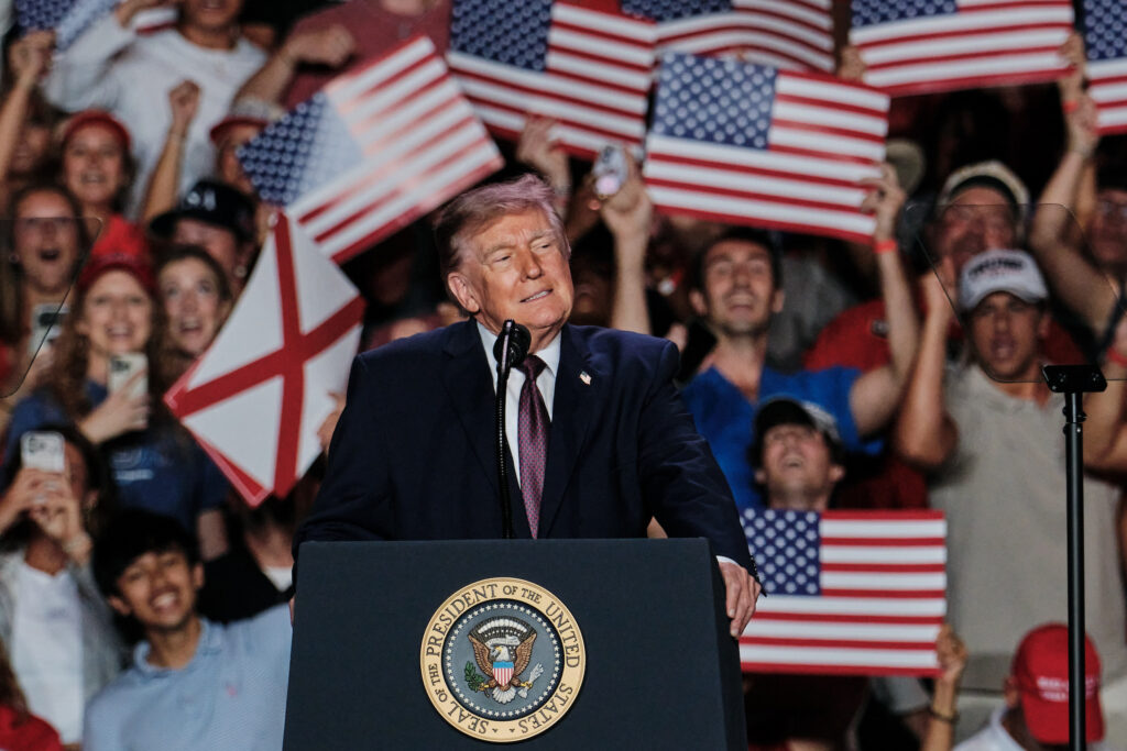 Donald Trump speaking at a rally with supporters holding American flags, promoting mail- — Trump encourages mail-in voting