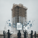 Silhouettes of people holding devices in front of a tall, partially constructed buil — Affordable Housing Construction Act